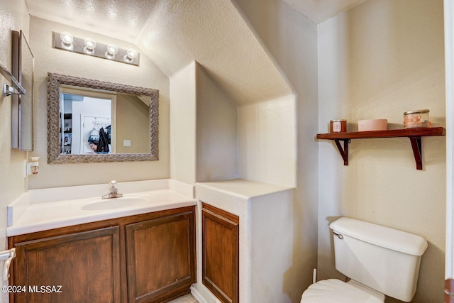 bathroom with lofted ceiling, a textured ceiling, toilet, and vanity