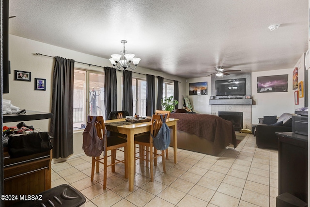 dining room with a textured ceiling, ceiling fan with notable chandelier, a tiled fireplace, and light tile flooring