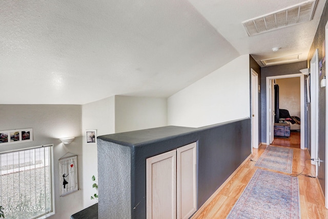 hall with lofted ceiling, a textured ceiling, and light hardwood / wood-style flooring