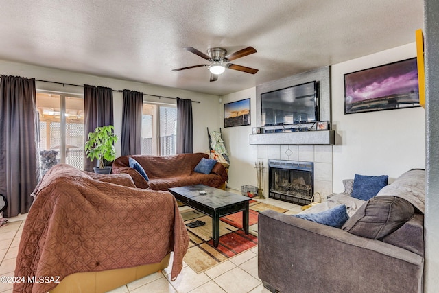 living room featuring ceiling fan, a textured ceiling, a large fireplace, and light tile floors