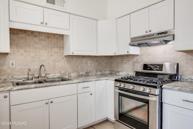 kitchen featuring stainless steel range with gas stovetop, light tile flooring, tasteful backsplash, white cabinetry, and sink