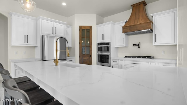 kitchen with white cabinets, custom exhaust hood, appliances with stainless steel finishes, and a breakfast bar area