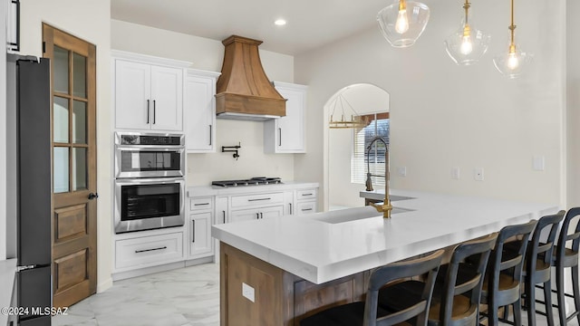 kitchen with appliances with stainless steel finishes, white cabinetry, a kitchen bar, custom range hood, and hanging light fixtures