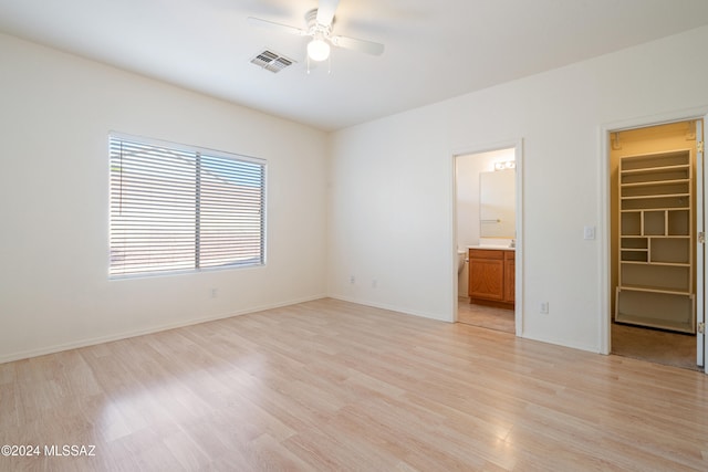 unfurnished bedroom featuring a walk in closet, ensuite bath, ceiling fan, light hardwood / wood-style floors, and a closet