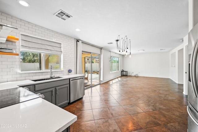 kitchen featuring gray cabinetry, a notable chandelier, sink, stainless steel appliances, and tasteful backsplash