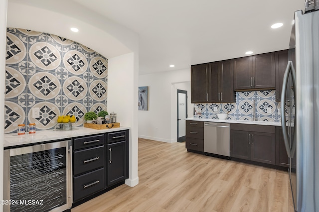 kitchen featuring dark brown cabinetry, stainless steel appliances, light hardwood / wood-style flooring, beverage cooler, and backsplash