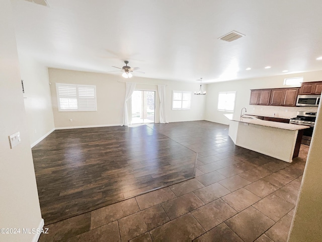 unfurnished living room with ceiling fan with notable chandelier, dark wood-type flooring, a sink, visible vents, and baseboards