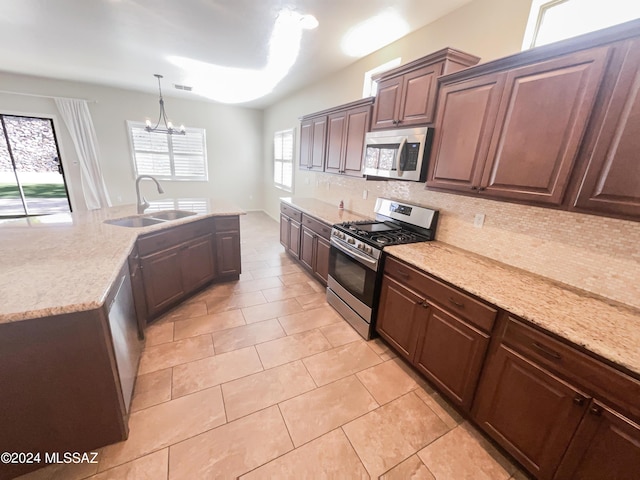 kitchen featuring tasteful backsplash, an inviting chandelier, appliances with stainless steel finishes, a sink, and light stone countertops