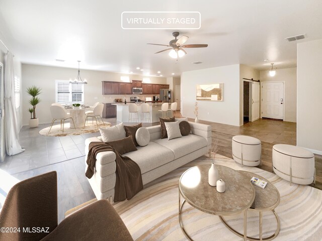 living room featuring a barn door, ceiling fan with notable chandelier, and light hardwood / wood-style floors