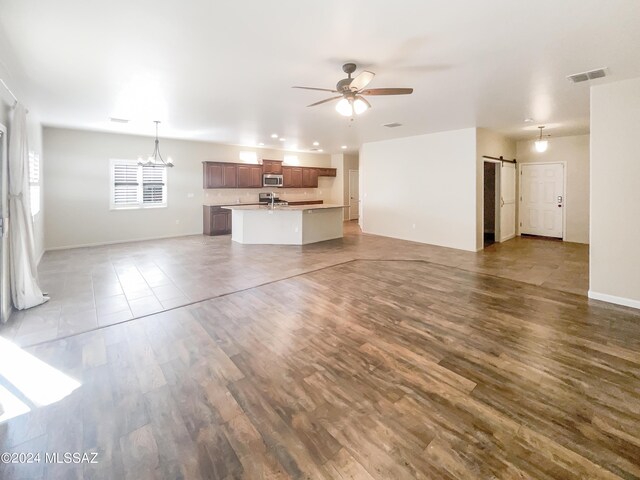 unfurnished living room featuring a barn door, ceiling fan with notable chandelier, and light hardwood / wood-style floors