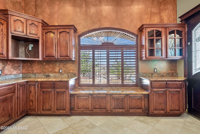 kitchen with light stone counters, a towering ceiling, and glass insert cabinets