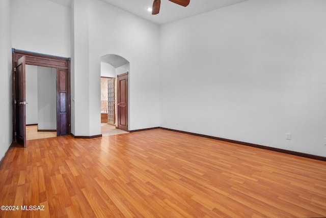 empty room with baseboards, light wood-style flooring, a high ceiling, ceiling fan, and arched walkways