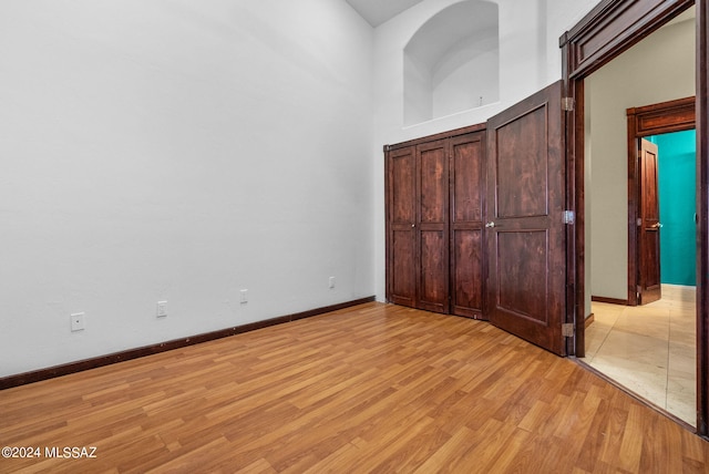 unfurnished bedroom with light wood-style flooring, a high ceiling, and baseboards