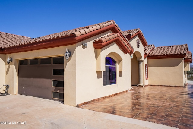 view of side of property featuring concrete driveway, stucco siding, a tiled roof, and an attached garage