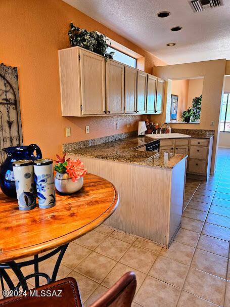 kitchen featuring kitchen peninsula, light brown cabinetry, a textured ceiling, light tile patterned floors, and dark stone countertops