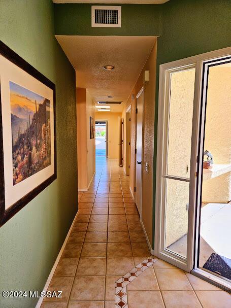 hall with light tile patterned floors, a textured ceiling, and a wealth of natural light