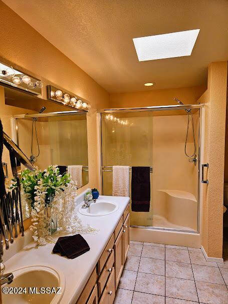 bathroom with tile patterned floors, a skylight, vanity, and a shower with shower door