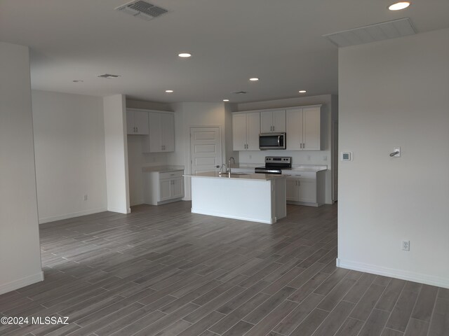 kitchen with sink, dark hardwood / wood-style flooring, stainless steel appliances, a center island with sink, and white cabinets