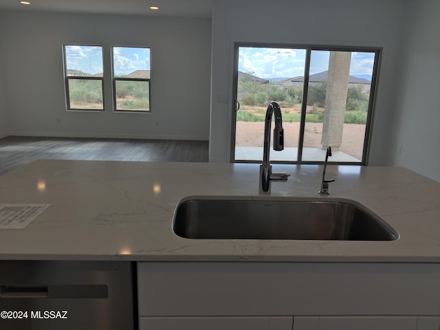 kitchen featuring light stone countertops, dishwasher, wood finished floors, white cabinets, and a sink