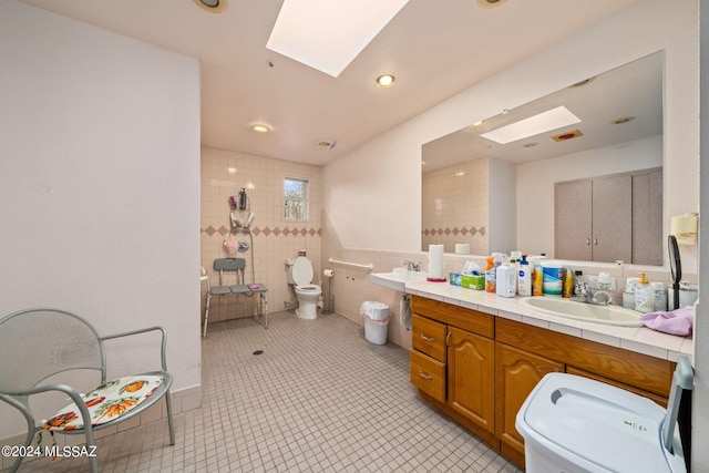 bathroom featuring tile flooring, tile walls, a skylight, toilet, and vanity