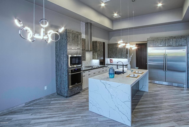 kitchen featuring a notable chandelier, built in appliances, an island with sink, and decorative light fixtures