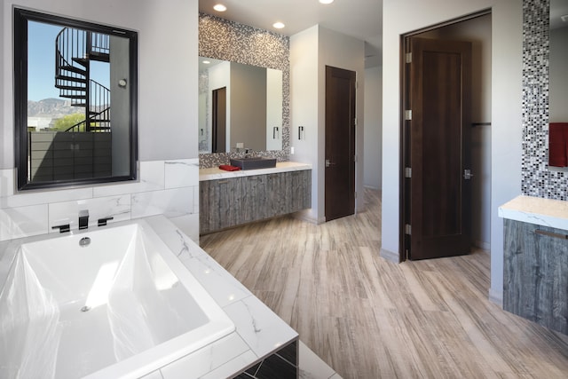 bathroom with a relaxing tiled bath and hardwood / wood-style floors