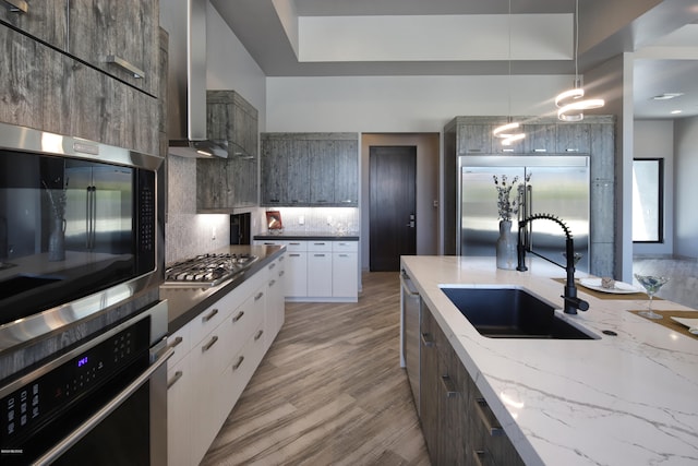 kitchen featuring pendant lighting, sink, appliances with stainless steel finishes, wall chimney exhaust hood, and tasteful backsplash