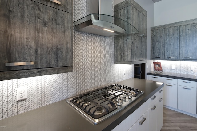 kitchen with wall chimney range hood, light hardwood / wood-style flooring, white cabinets, backsplash, and stainless steel gas cooktop