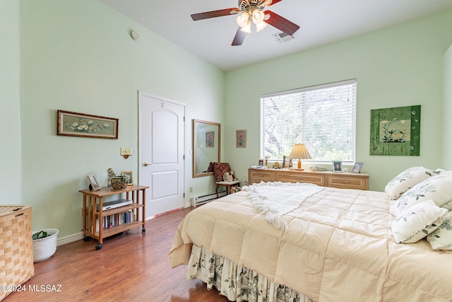 bedroom featuring dark hardwood / wood-style flooring, ceiling fan, and a baseboard heating unit