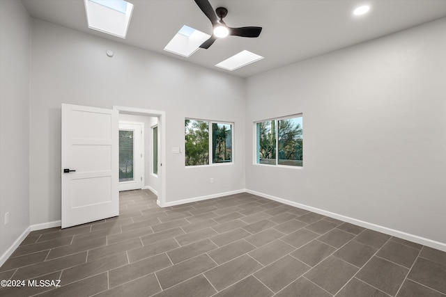 tiled spare room featuring a skylight, ceiling fan, and a high ceiling