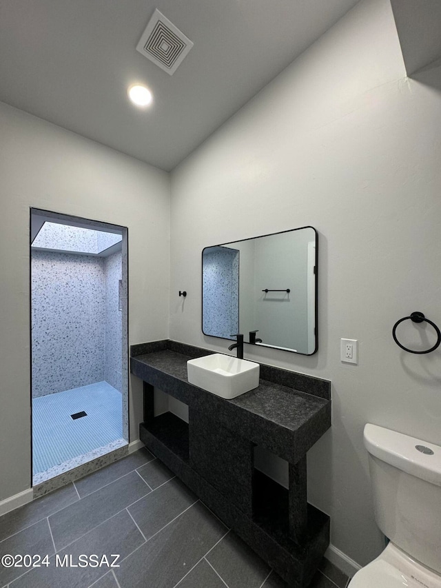 bathroom with tiled shower, tile patterned floors, toilet, and vanity