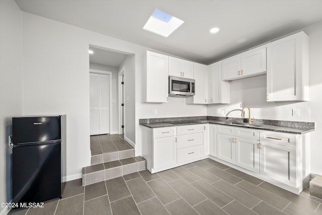 kitchen with black appliances, dark tile patterned floors, white cabinets, a skylight, and sink