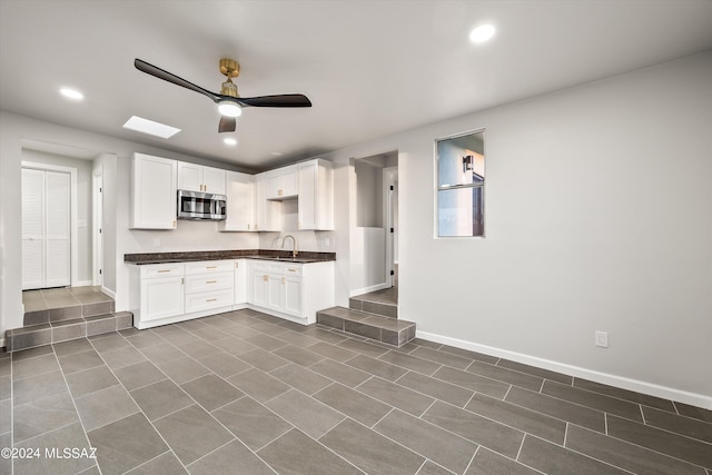 kitchen with a skylight, dark tile patterned floors, white cabinets, ceiling fan, and sink