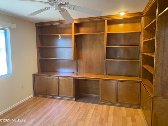 unfurnished office with built in desk, ceiling fan, plenty of natural light, and light hardwood / wood-style flooring