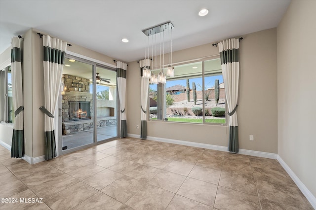 empty room with a stone fireplace, ceiling fan, and light tile patterned flooring