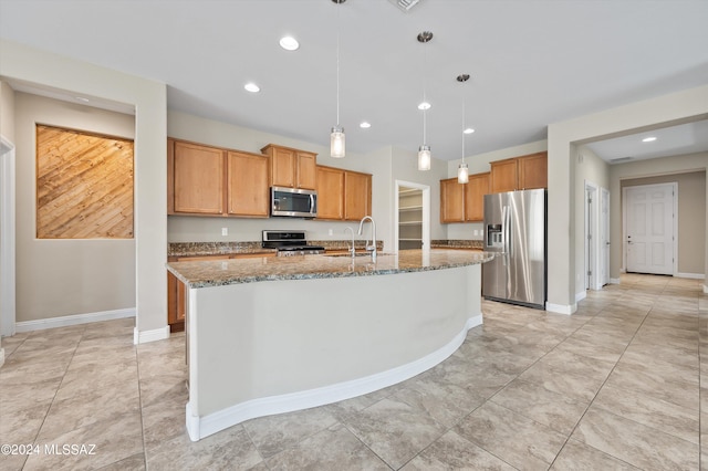 kitchen with pendant lighting, sink, appliances with stainless steel finishes, dark stone countertops, and a center island with sink