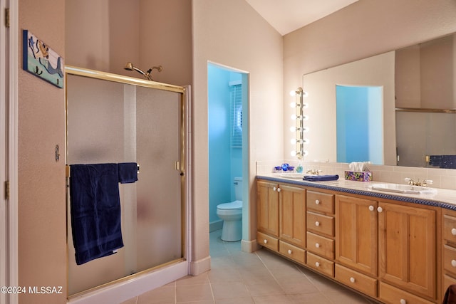 bathroom featuring tile floors, a shower with shower door, dual sinks, toilet, and vanity with extensive cabinet space