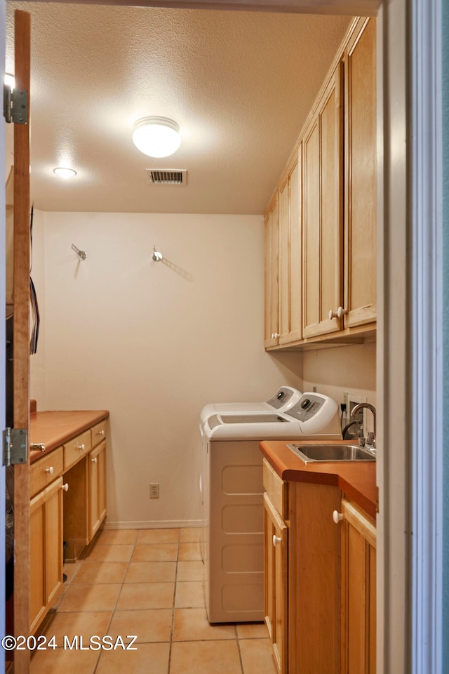 clothes washing area featuring cabinets, sink, light tile floors, a textured ceiling, and independent washer and dryer