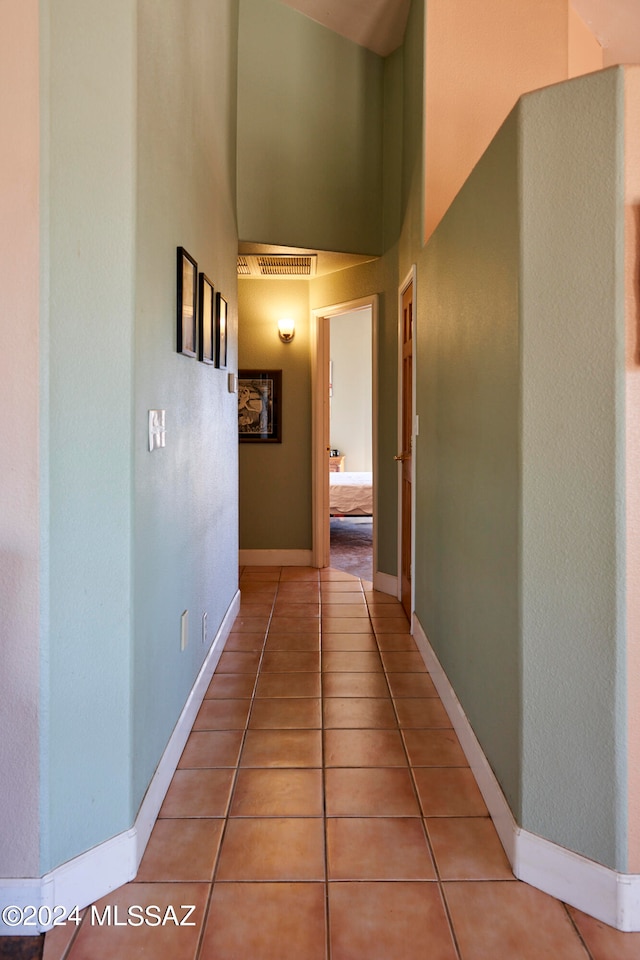 hall featuring light tile floors and a towering ceiling