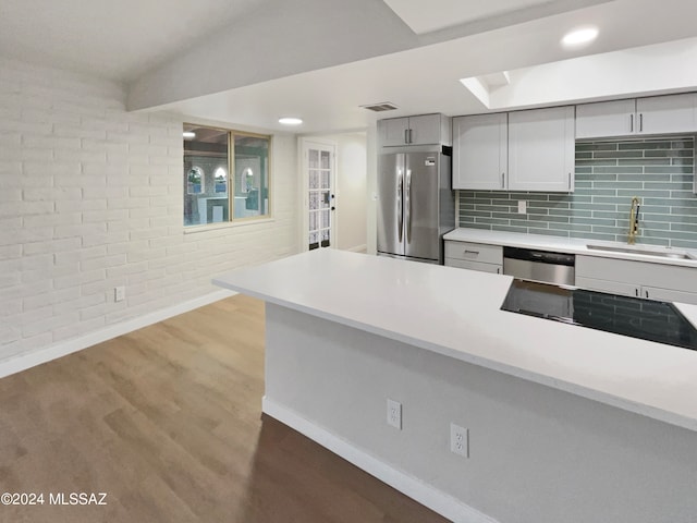 kitchen with tasteful backsplash, appliances with stainless steel finishes, sink, kitchen peninsula, and hardwood / wood-style flooring