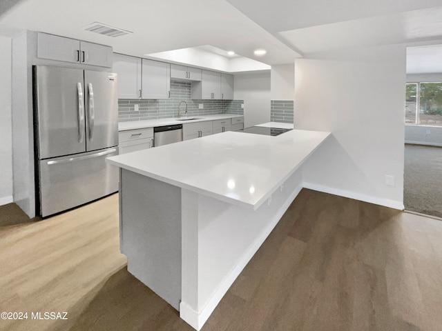 kitchen with kitchen peninsula, decorative backsplash, appliances with stainless steel finishes, light colored carpet, and sink