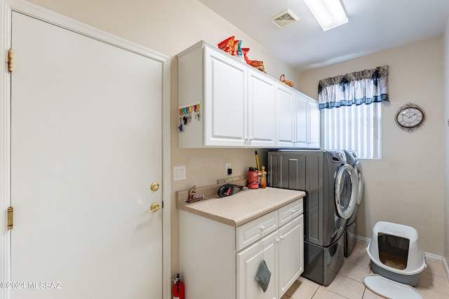 clothes washing area featuring washing machine and clothes dryer, light tile patterned floors, and cabinets