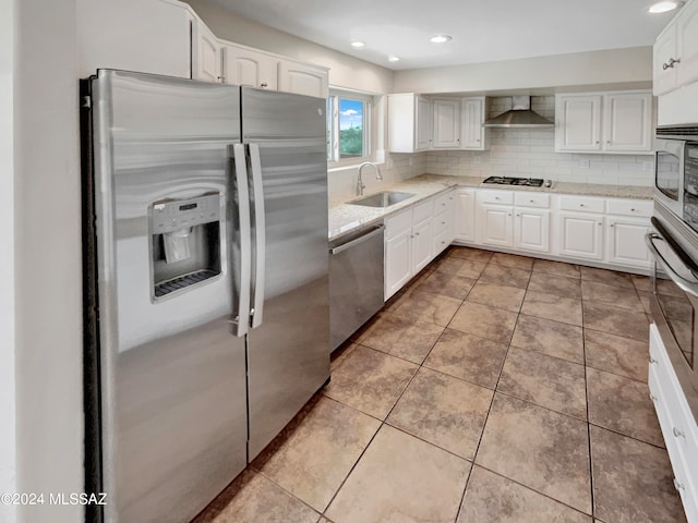 kitchen featuring wall chimney exhaust hood, white cabinetry, appliances with stainless steel finishes, backsplash, and sink