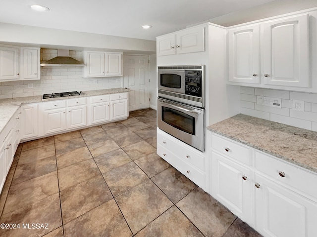 kitchen with backsplash, appliances with stainless steel finishes, light stone counters, and wall chimney exhaust hood