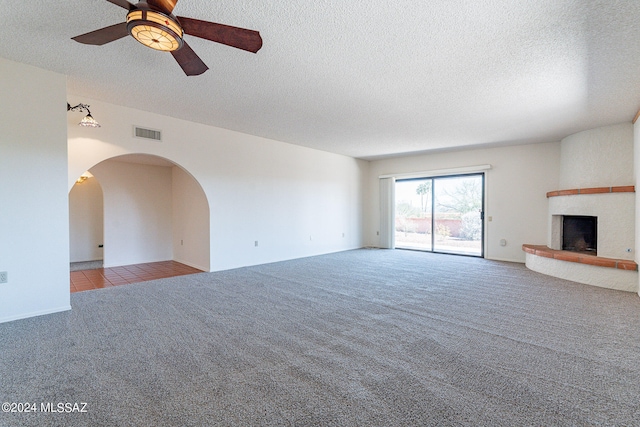 unfurnished living room featuring a textured ceiling, ceiling fan, carpet floors, and a fireplace