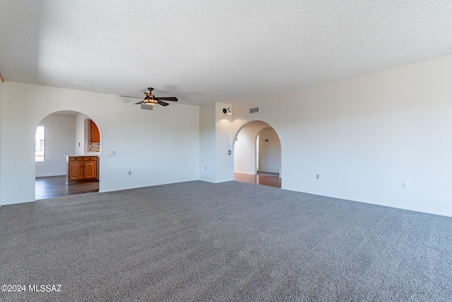 spare room featuring ceiling fan, dark carpet, and a textured ceiling