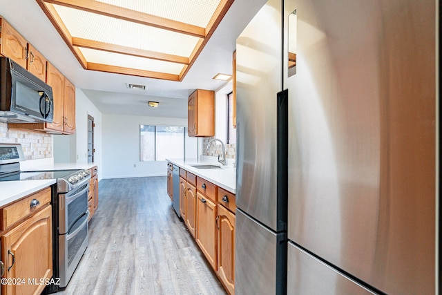 kitchen with appliances with stainless steel finishes, sink, tasteful backsplash, and light wood-type flooring