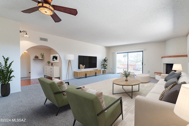 living room with light carpet, ceiling fan, a textured ceiling, and a fireplace