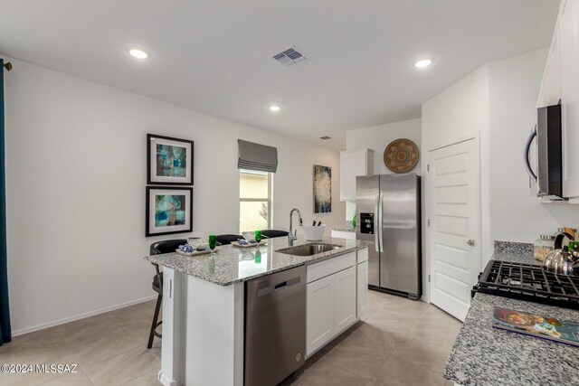 kitchen featuring white cabinets, light stone countertops, stainless steel appliances, a center island with sink, and sink