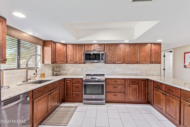 kitchen featuring stainless steel appliances, sink, light stone counters, backsplash, and a raised ceiling